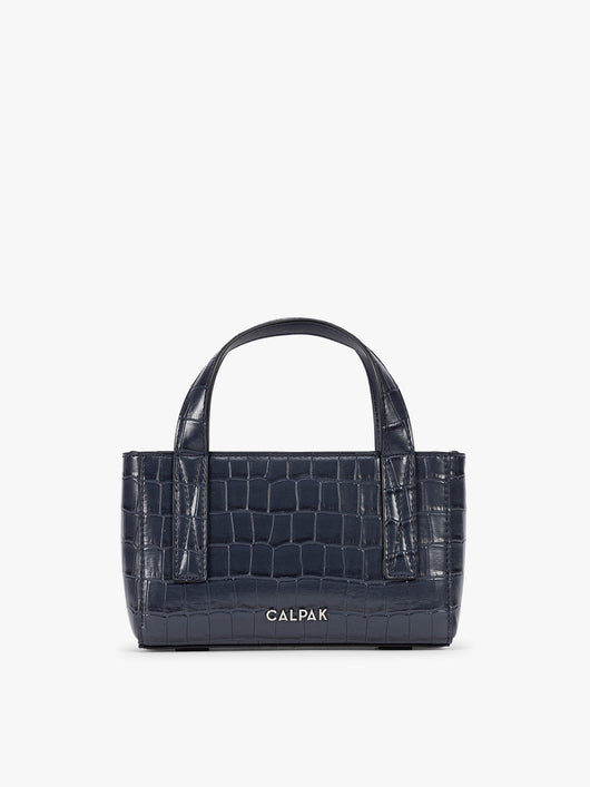 A CALPAK Haven Mini Crossbody Bag in Navy blue crocodile-embossed with top handles on a plain white background; AMC2502-NAVY-FAUX-CROC