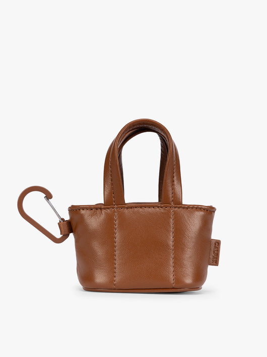 A small light brown Honey Brown CALPAK Luka Tote Bag Charm with dual top handles and a black carabiner clip attached to the side, shown against a plain white background; AMT2601-HONEY-BROWN-PU