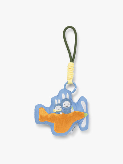 Plush Miffy x CALPAK Pluffy Bag Charm keychain with a blue border and Miffys holding a carrot on an orange airplane with a white background;APLF2501-MIFFY-ON-THE-WAY