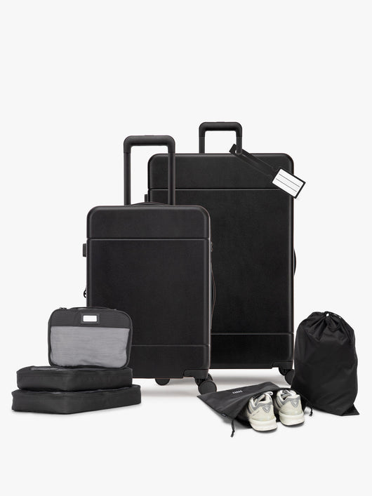 Opened CALPAK Hue Starter Bundle in Black that comes with Large and Carry On Luggage, Luggage Tag, Two Black Pouches, and Three Black Packing Cubes shown on a white background; LHU8000-BLACK