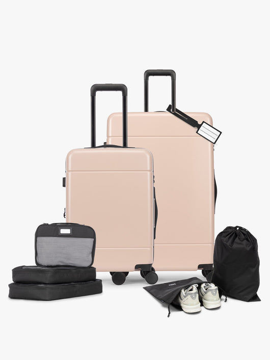 Opened CALPAK Hue Starter Bundle in light pink Rose Quartz that comes with Large and Carry On Luggage, Luggage Tag, Two Black Pouches, and Three Black Packing Cubes shown on a white background; LHU8000-ROSE-QUARTZ