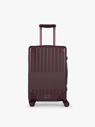CALPAK Vault deep red Dark Cherry hard-shell spinner Carry On Luggage with a telescoping handle extended, featuring a deep red leatherette side handle and trim, set against a plain light gray background; LVT1020-DARK-CHERRY