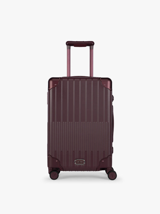 CALPAK Vault deep red Dark Cherry hard-shell spinner Carry On Luggage with a telescoping handle extended, featuring a deep red leatherette side handle and trim, set against a plain light gray background; LVT1020-DARK-CHERRY