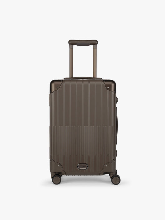 CALPAK Vault brown Mushroom hard-shell spinner Carry On Luggage with a telescoping handle extended, featuring a black leatherette side handle and trim, set against a plain light gray background; LVT1020-MUSHROOM