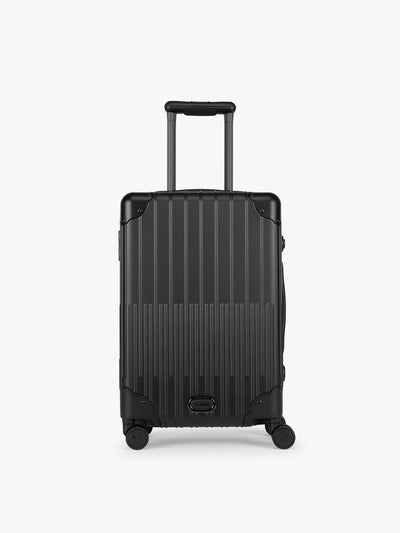 CALPAK Vault black Onyx hard-shell spinner Carry On Luggage with a telescoping handle extended, featuring a Black leatherette side handle and trim, set against a plain light gray background; LVT1020-ONYX