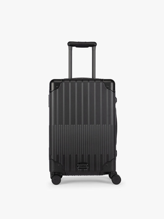 CALPAK Vault black Onyx hard-shell spinner Carry On Luggage with a telescoping handle extended, featuring a Black leatherette side handle and trim, set against a plain light gray background; LVT1020-ONYX