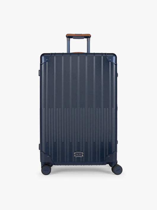 CALPAK Large Vault Luggage in blue Navy with hard-shell spinner suitcase with a ribbed vertical design, shown from the front on a light gray background; LVT1028-NAVY