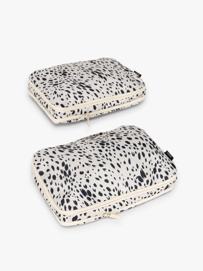 Two white and black animal print Snow Leopard CALPAK Medium Compression Packing Cubes with zippers shown on a clean white background; PCC2201-SNOW-LEOPARD