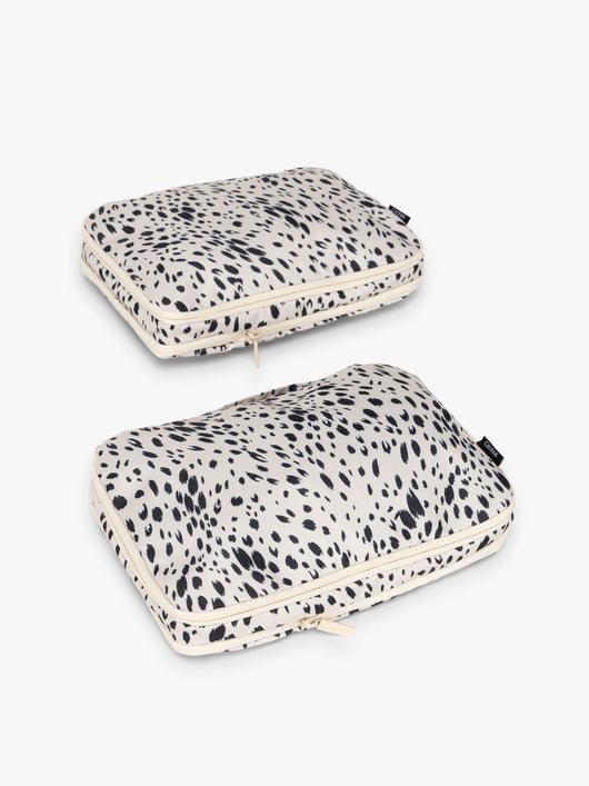 Two white and black animal print Snow Leopard CALPAK Medium Compression Packing Cubes with zippers shown on a clean white background; PCC2201-SNOW-LEOPARD